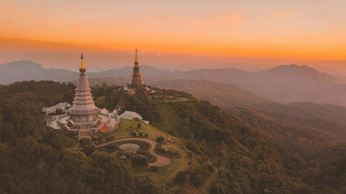 The two royal pagodas of Doi Inthanon on a forested ridge at golden hour, mountains fading into the distance