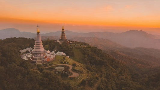 The two royal pagodas of Doi Inthanon on a forested ridge at golden hour, mountains fading into the distance